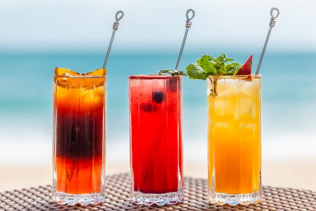 Conjunto de coquetéis de frutas refrescantes em pé na mesa na praia perto do mar turquesa