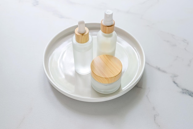 Conjunto de cosméticos de cuidados faciais Garrafas de cosméticos em branco com tampas de bambu na bandeja de cerâmica na mesa de mármore Natural Orgânico Spa Cosmético Beleza Conceito Design Mock up