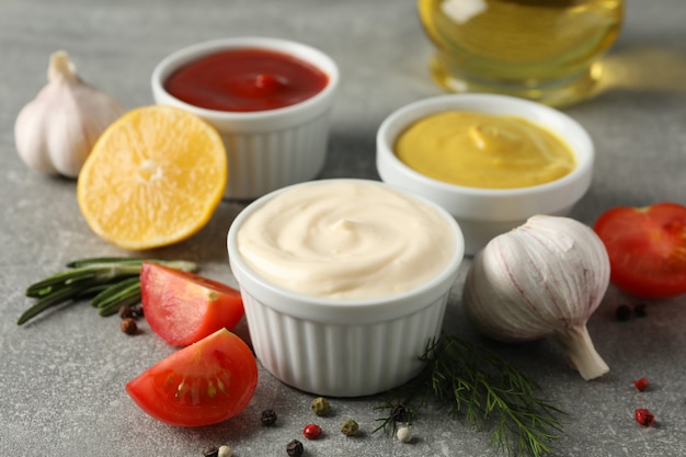 Conjunto de diferentes deliciosos molhos, alho, tomate cereja, azeite de oliva no fundo cinza, closeup. Espaço para texto