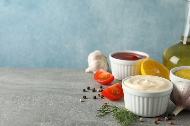 Conjunto de diferentes deliciosos molhos, alho, tomate cereja, limão em fundo cinza, espaço para texto