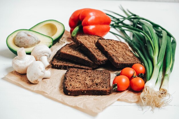 Conjunto de diferentes legumes frescos com fatias de pão integral em um fundo branco de mesa de madeira. Copie, espaço vazio para texto