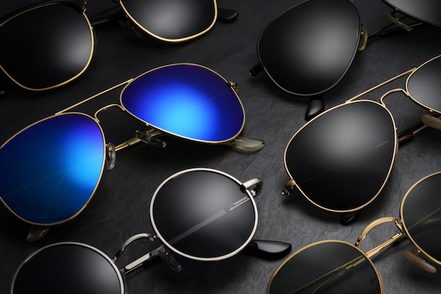 Conjunto de diferentes óculos de sol dispostos em uma fileira sobre fundo preto de ardósia