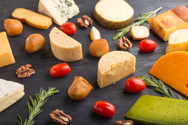 Conjunto de diferentes tipos de queijo com alecrim e tomate em uma superfície de madeira preta
