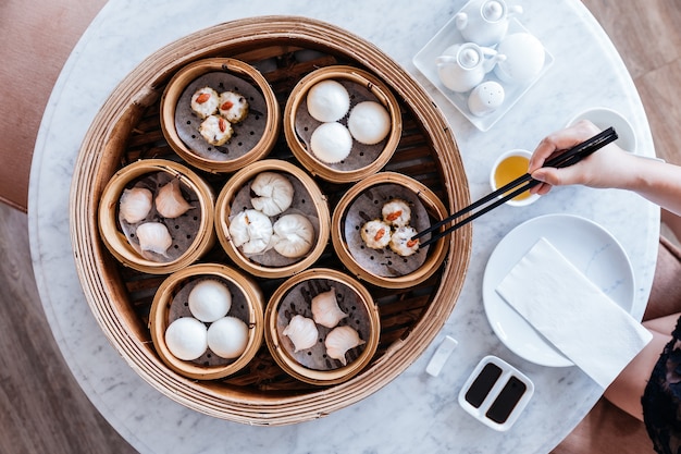 Conjunto de dim sum servido em cestas de vapor com mão usando pauzinhos.