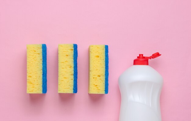 Foto conjunto de donas de casa para lavar louça. lava-louças. garrafa de utensílios de lavagem, esponjas em fundo rosa. vista do topo.
