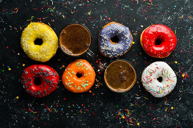 Conjunto de donuts coloridos doces com uma xícara de café em uma mesa de pedra preta Vista superior Flat Lay