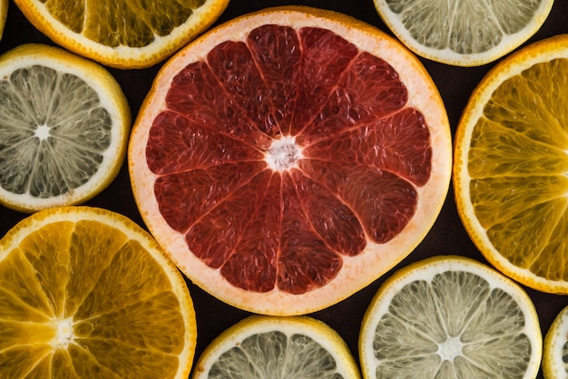 Conjunto de fatias de frutas cítricas em fundo escuro: laranja, limão, toranja.