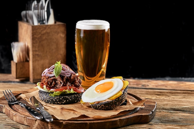 Conjunto de hambúrguer com ovo e cerveja. Um conjunto padrão de bebidas e comidas no bar, cerveja e petiscos. Fundo escuro, fast food. Comida tradicional americana.