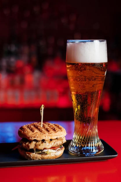 Conjunto de hambúrguer e cerveja Bebida e lanche na barra vermelha Fast food Um hambúrguer com carne e um copo de cerveja