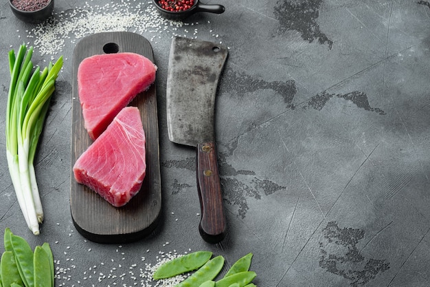 Conjunto de ingredientes de bife de atum com gergelim cru, na tábua de madeira e uma velha faca de cutelo de açougueiro, na mesa de pedra cinza
