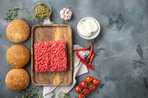 Conjunto de ingredientes de hambúrgueres de carne picada crua em casa, em uma bandeja de madeira, em uma mesa de pedra cinza, vista de cima plana