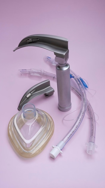 conjunto de intubação - laringoscópio e tubos endotraqueais para ventilador deitado em fundo rosa