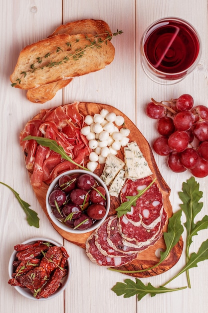 Conjunto de lanche de vinho. variedade de queijo e carne, azeitonas, uvas, rúcula no fundo branco