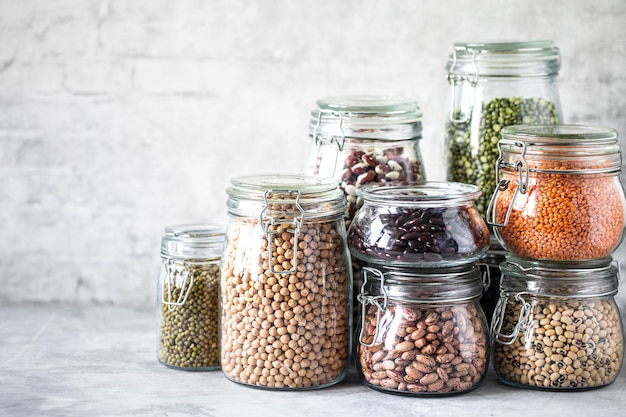 Conjunto de legumes diferentes em frascos de vidro, mesa branca de concreto. Uma fonte de proteína para vegetarianos. O conceito de alimentação saudável e armazenamento de alimentos.