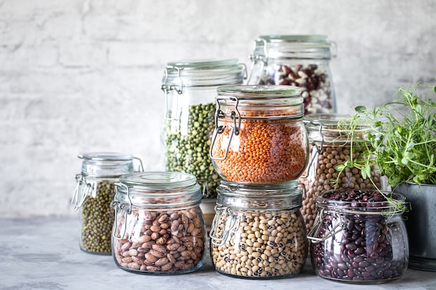 Conjunto de legumes diferentes em frascos de vidro, mesa branca de concreto. Uma fonte de proteína para vegetarianos. O conceito de alimentação saudável e armazenamento de alimentos.