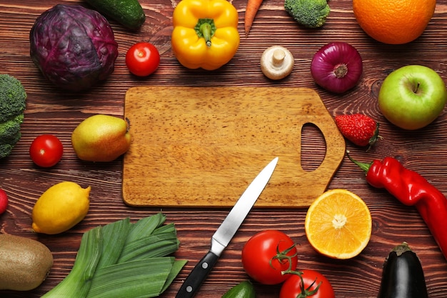 Conjunto de legumes e frutas frescos com prancha de cortar em fundo de madeira