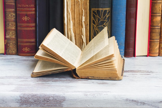 Conjunto de livros antigos com um aberto em mesa de madeira branca