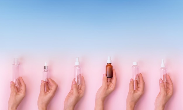 Conjunto de mãos segurando diferentes frascos de cosméticos em fundo rosa desfocado com espaço de cópia