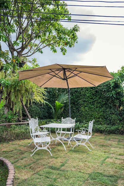 Conjunto de mesa branca com cadeiras e guarda-chuva no jardim no quintal