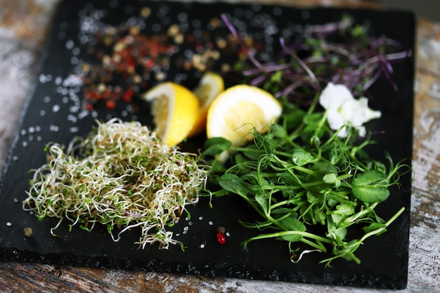 Conjunto de microgreens e especiarias em uma placa de pedra preta.