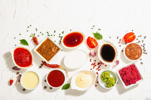 Conjunto de molhos diferentes - ketchup, maionese, churrasco, soja, chutney, wasabi, adjika, raiz-forte, aioli, marinara. luz dura na moda, sombra escura. fundo de massa branca, vista superior