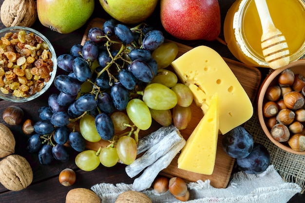 Conjunto de outono de produtos uvas nozes avelãs ameixas mel queijo passas peras cranberries secas na mesa de madeira