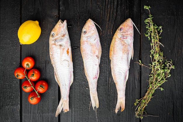 Conjunto de peixes de frutos do mar inteiros surmullet crus, com ingredientes e ervas, no fundo preto da mesa de madeira, vista superior plana lay