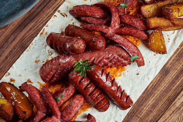 Conjunto de petiscos de cerveja - salsichas assadas, couve cozida e batatas em uma placa de madeira. Fotografia de alimentos