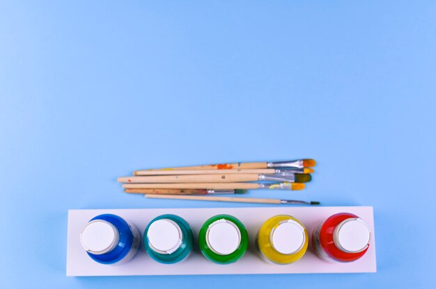 conjunto de pincéis de artista plana com dicas desenhadas sobre fundo azul e latas de tinta