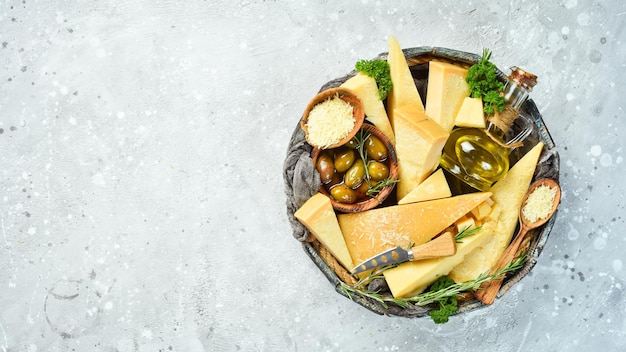 Conjunto de queijos duros em uma cesta de madeira Queijo parmesão cortado em pedaços Queijo Vista superior Em um fundo de pedra cinza