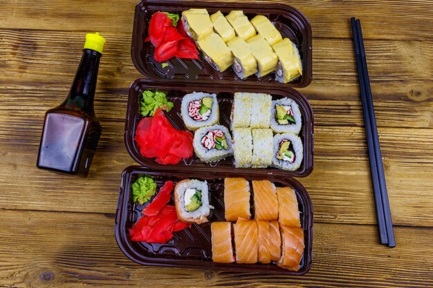 Conjunto de rolos de sushi em caixas de plástico molho de soja e pauzinhos na mesa de madeira Vista superior