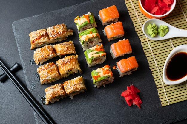 Conjunto de rolos de sushi fresco com enguia, abacate e salmão na placa de ardósia preta.