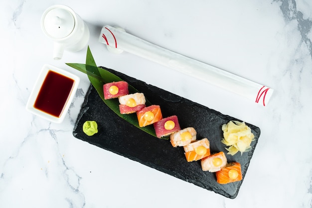 Conjunto de rolos de sushi servidos em uma folha de bananeira em uma pedra preta sobre uma mesa de mármore com pauzinhos e molho de soja. comida japonesa sushi de camarão com salmão e atum. marisco saudável.