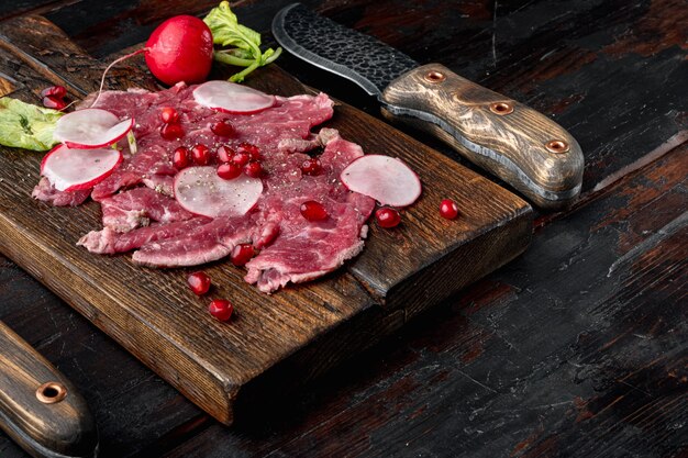 Conjunto de salada de carpaccio fresco com vinagre de vinho, rabanete e granada, em uma tábua de servir de madeira, no fundo da velha mesa de madeira escura, com espaço de cópia para o texto