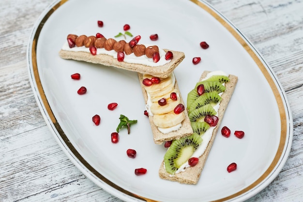 Conjunto de sanduíches orgânicos da estação em pães estaladiços secos de grãos marrons com legumes frescos frutas maduras creme de queijo na vista superior da mesa de madeira branca