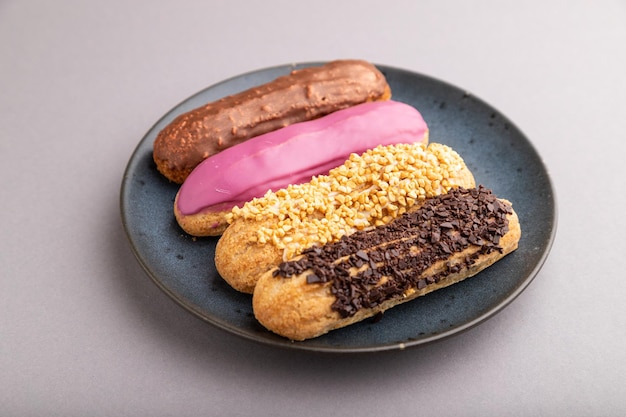 Conjunto de sobremesa francesa tradicional éclair em placa de cerâmica azul sobre fundo cinza pastel vista lateral de perto