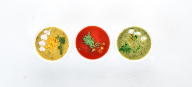 Conjunto de sopas de legumes quentes e coloridas. Sopa de brócolis, milho, sopa de tomate. Comida saudável. Em um fundo branco de madeira. Copie o espaço.