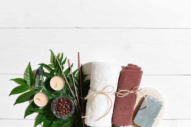 Conjunto de spa com toalha e sabonete em fundo branco de madeira com folhas verdes