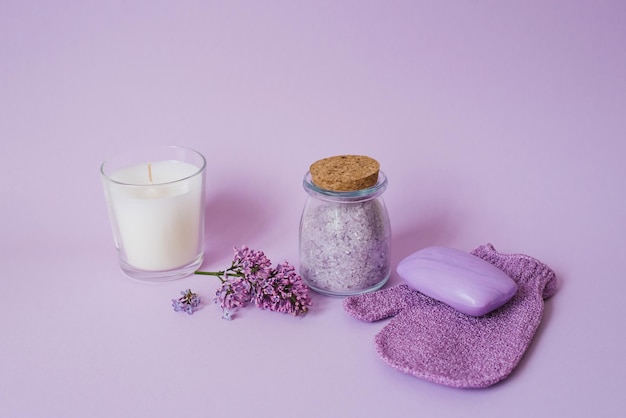 Conjunto de spa cosmético para cuidados com o corpo Sal marinho em frasco de vidro luva de toalha de sabão orgânico e flores lilás em fundo roxo