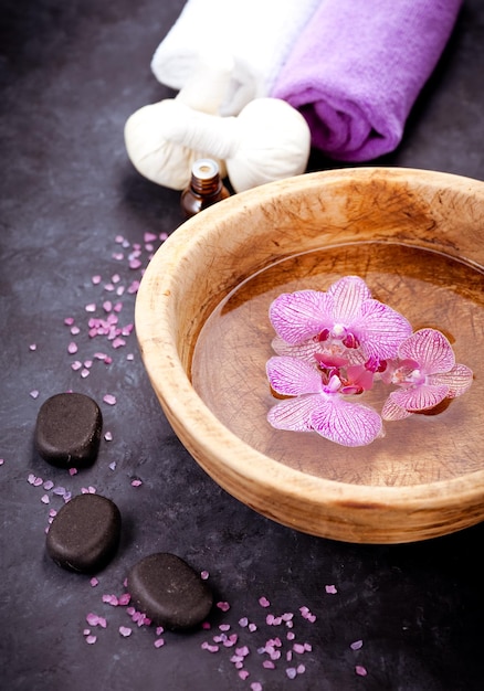 Conjunto de spa Flores de orquídea em uma tigela com toalhas de pedras zen de água e óleos de massagem