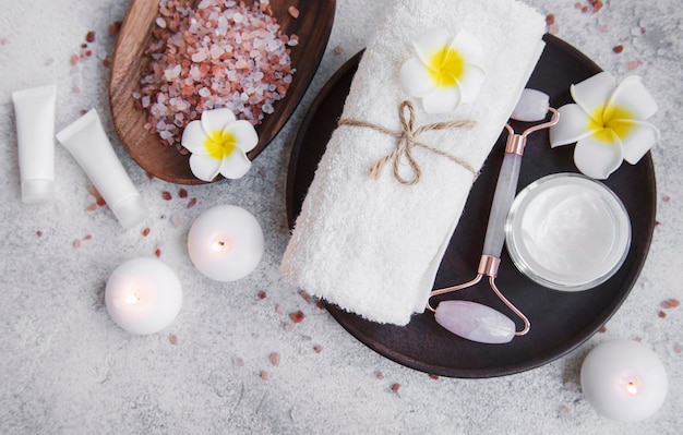 Conjunto de spa, óleo essencial, sal de massagem, velas e flores de frangipani em fundo cinza de concreto