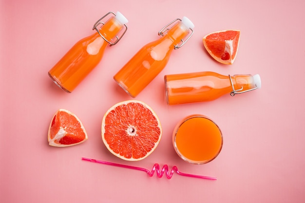 Conjunto de suco de toranja espremido na hora, em plano de fundo rosa texturizado de verão, vista superior plana