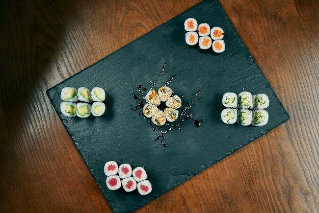 Conjunto de sushi maki roll com pepino, salmão, enguia, atum na placa preta sltae na mesa de madeira. cozinha japonesa. vista do topo