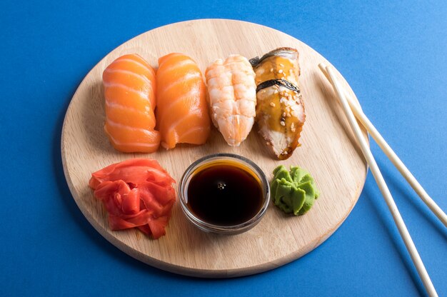 Conjunto de sushi nigiri apetitoso delicioso servido em placas de madeira com molho de soja e pauzinhos. Postura plana na mesa azul