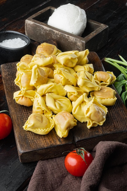 Conjunto de tortellini caseiro com queijo e manjericão, numa tábua de madeira, no fundo da velha mesa de madeira escura