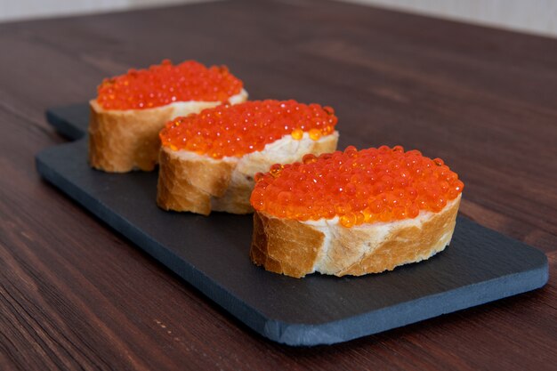 Conjunto de três sanduíches com caviar vermelho na placa de pedra cinza