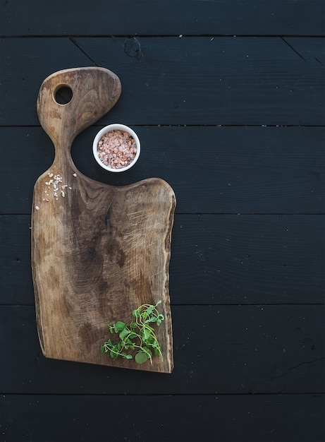 Conjunto de utensílios de cozinha. Velha tábua rústica feita de madeira de nogueira, sal e orégano erva em uma mesa preta, vista superior
