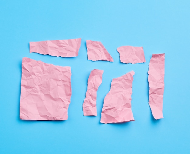 Conjunto de vários pedaços de papel amassado rosa sobre uma superfície azul