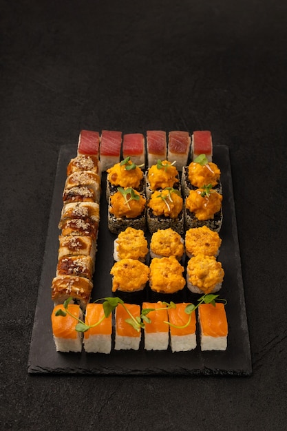 Conjunto de vários rolos de sushi comida japonesa em uma placa preta para servir em um fundo preto