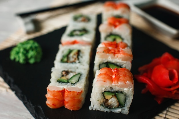 Conjunto de deliciosos rollos de sushi con camarones servidos en primer plano de pizarra negra. Foto de menú de restaurante japonés de lujo.